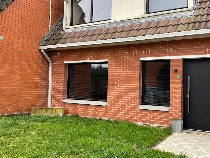 Façade latérale d'une maison en briques rouges avec fenêtres et porte noire